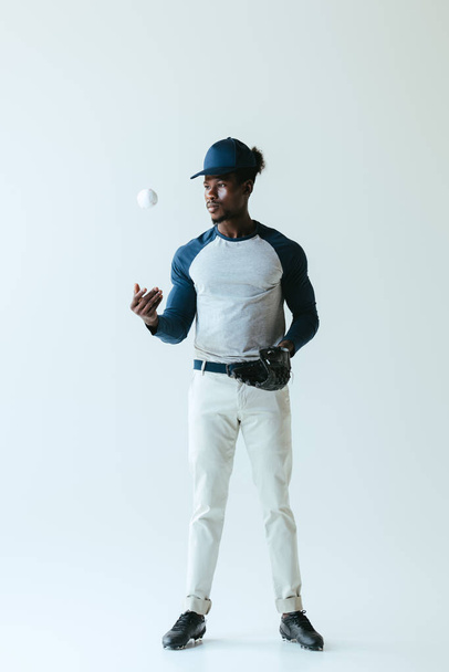 handsome african american sportsman in baseball glove playing with ball on grey background - Foto, afbeelding