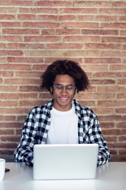 Handsome young afro-american man with eyeglasses using his laptop at home. - Fotoğraf, Görsel