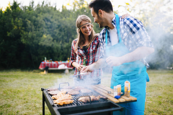 Young happy people enjoying barbecuing in forest - 写真・画像
