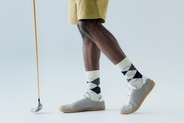灰色の背景にゴルフクラブを保持しているアフリカ系アメリカ人のスポーツマンのトリミングビュー - 写真・画像