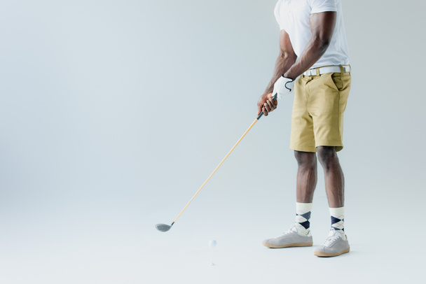 κομμένη θέα του αφρικανικού αμερικανικού αθλητή σε σορτς παίζοντας γκολφ σε γκρίζο φόντο - Φωτογραφία, εικόνα