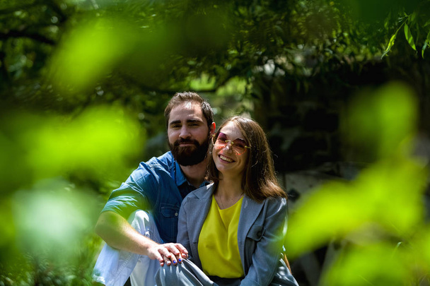 A fiatal és modern szerető pár a park zöldje között ül. pozitív érzelmekkel. Boldogság. Család. - Fotó, kép