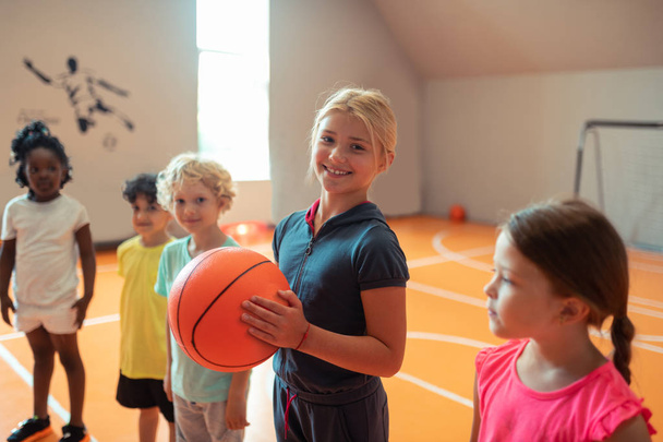 Smiling girl holding a ball standing next to her classmates. - Φωτογραφία, εικόνα