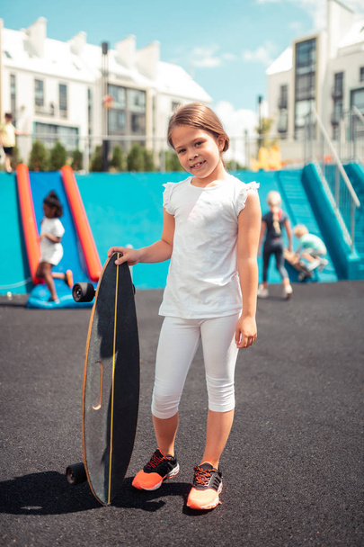 Smiling girl standing with her skateboard outside. - Zdjęcie, obraz