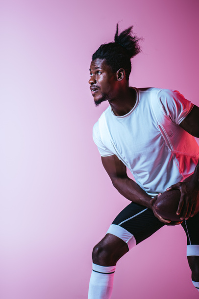 przystojny African American sportowca grając w futbol amerykański na fioletowym tle z gradientem - Zdjęcie, obraz