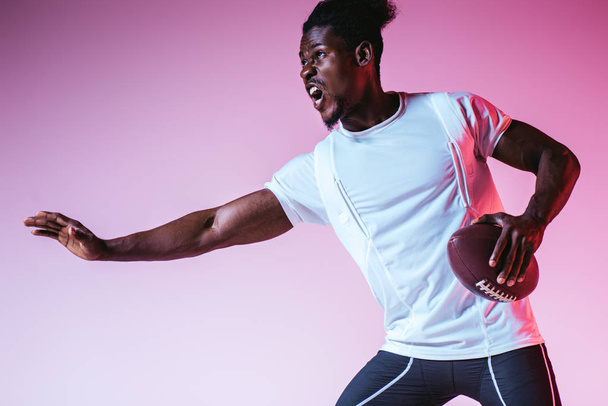 excited african american sportsman playing american football on purple background with gradient - Foto, immagini