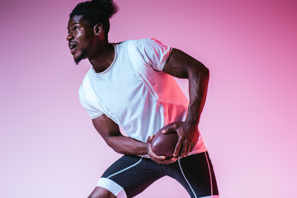 excited african american sportsman playing american football on purple background with gradient - Foto, imagen