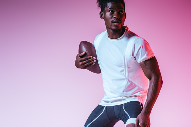 pohledný africký americký sportovec hrající americký fotbal na purpurovém pozadí s přechodem - Fotografie, Obrázek