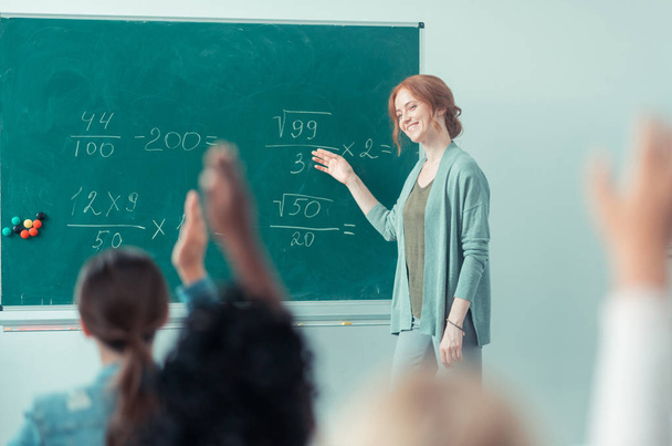 Teacher explaining sums standing near the blackboard. - Фото, изображение