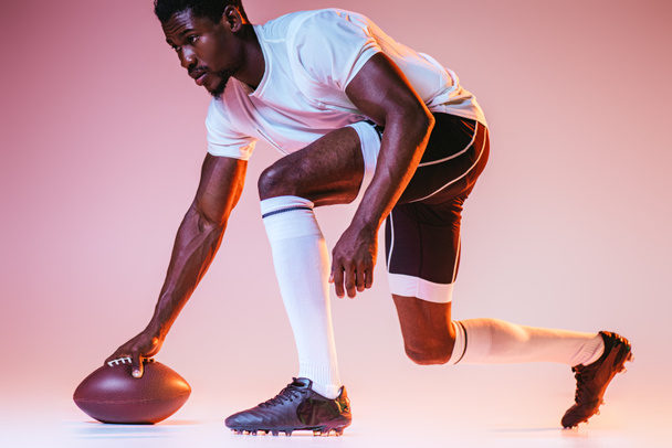 young african american sportsman playing american football on pink background with gradient and yellow lighting - Fotografie, Obrázek