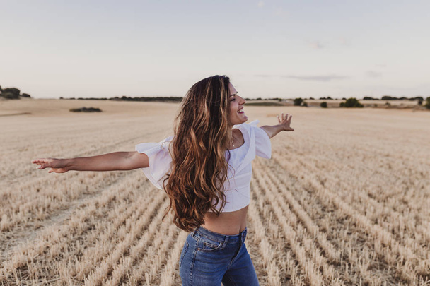 Summer Girl enjoying nature on yellow field. Beautiful young woman dancing Outdoors. Long hair in the wind. Happiness and lifestyle. Back view - Фото, зображення