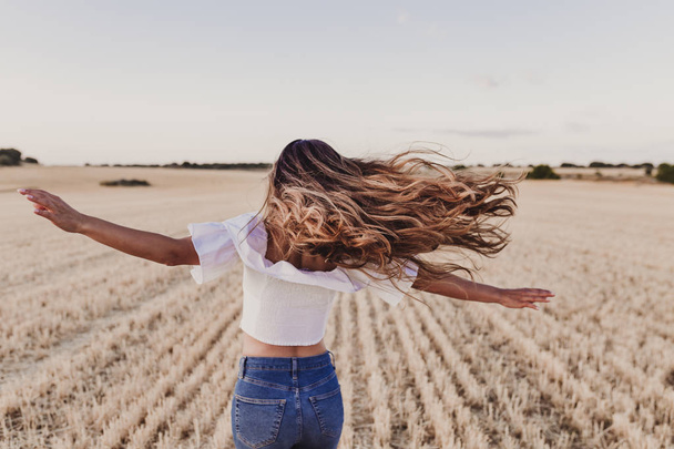Summer Girl enjoying nature on yellow field. Beautiful young woman dancing Outdoors. Long hair in the wind. Happiness and lifestyle. Back view - Photo, Image