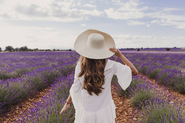 charming Young woman with a hat and white dress in a purple lavender field at sunset. LIfestyle outdoors. Back view - Foto, imagen