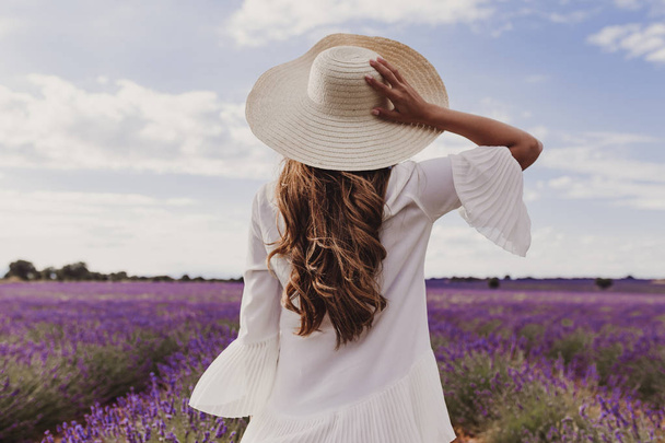 charming Young woman with a hat and white dress in a purple lavender field at sunset. LIfestyle outdoors. Back view - Valokuva, kuva
