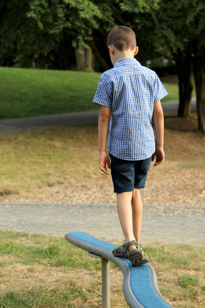 boy schoolboy in shorts walks on a horizontal sports game projectile on a playground in a park in summer, training coordination and body balance - Foto, imagen