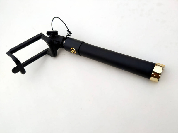 Uma vara selfie extensível com uma braçadeira ajustável na extremidade em um fundo branco
 - Foto, Imagem