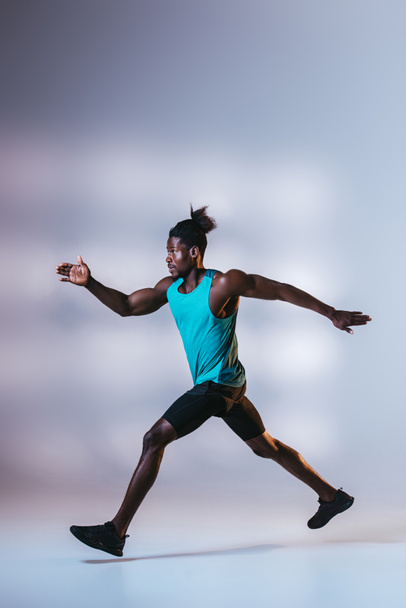 young african american sportsman running on grey background with lighting - Φωτογραφία, εικόνα