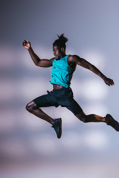 young, athletic african american sportsman jumping on grey background with lighting - Photo, Image