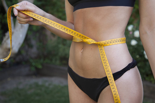 Slim woman holding a measuring tape around her waist. Diet concept - 写真・画像