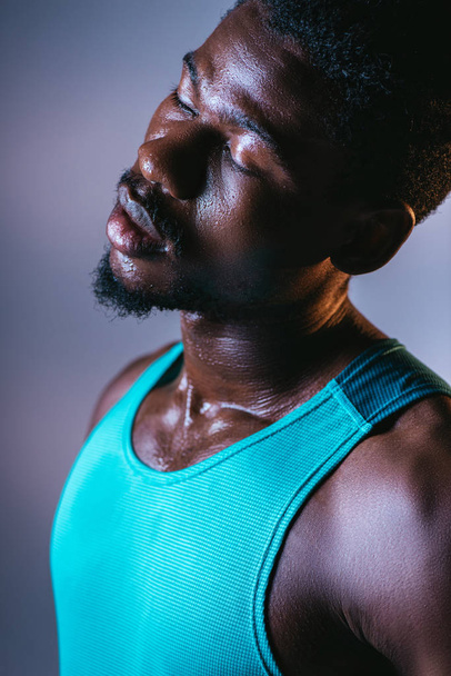 portrét afrického amerického sportovce se zpocenou tváří a zavřenýma očima na šedém pozadí s osvětlením - Fotografie, Obrázek