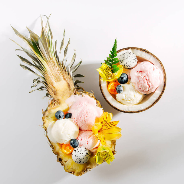 Balls of ice cream decorated flowers and berries in halves of coconuts and pineapples - Foto, imagen