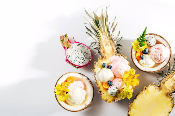 Balls of ice cream decorated flowers and berries in halves of coconuts and pineapples - Foto, immagini