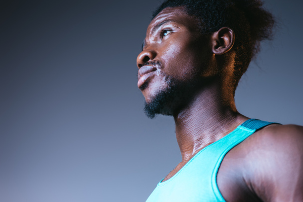 handsome, confident african american sportsman looking away on grey background with lighting - Photo, Image