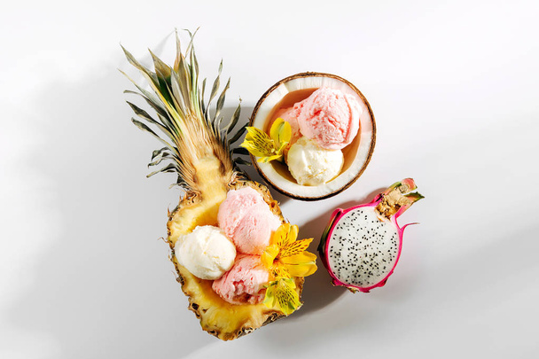 Balls of ice cream decorated flowers and berries in halves of coconuts and pineapples - Photo, image