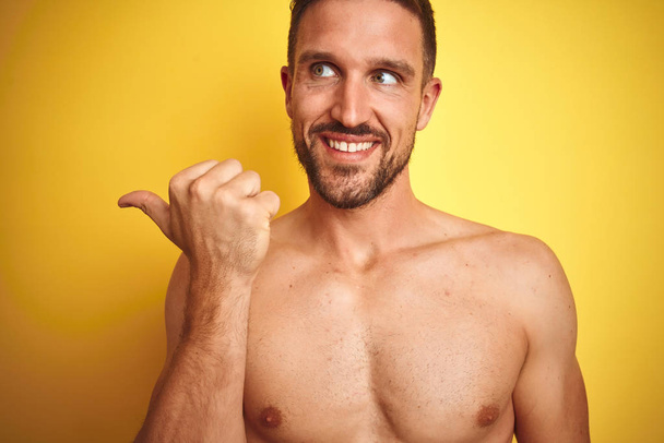 Seksi genç gömleksiz adam sarı izole arka plan üzerinde çıplak Fitness göğüs gösteren mutlu yüz görünümlü ve başparmak ile yan işaret. - Fotoğraf, Görsel