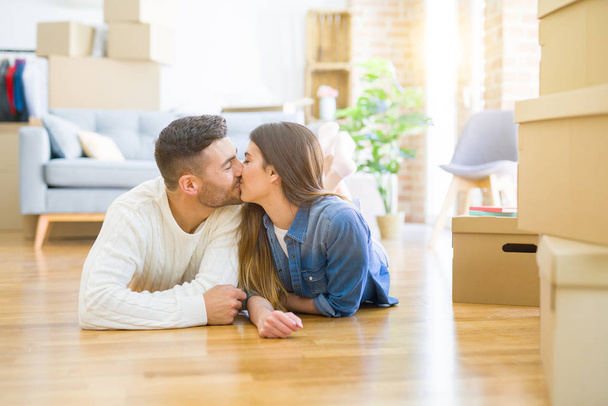 新しい家の床に横たわっている若い美しいカップルは、新しいアパートに引っ越すために非常に幸せに恋に微笑む - 写真・画像
