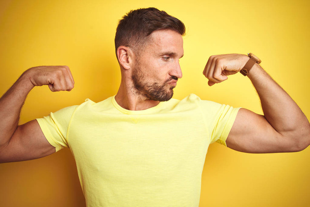 Young handsome man wearing casual yellow t-shirt over yellow isolated background showing arms muscles smiling proud. Fitness concept. - Φωτογραφία, εικόνα