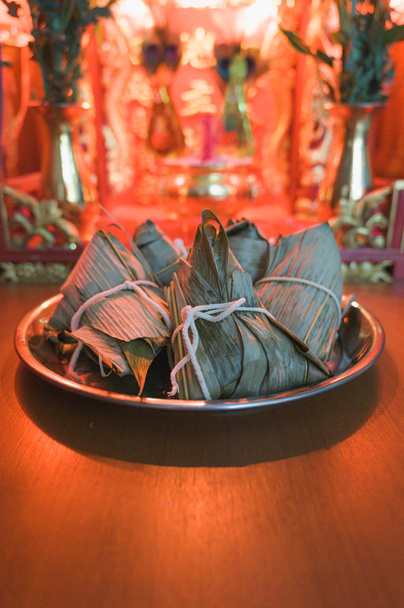 Closeup Bolinho de arroz pegajoso ou Zongzi em bandeja de aço inoxidável na frente da casa do espírito chinês durante o Dragon Boat Festival. Preste respeito ao antepassado
. - Foto, Imagem