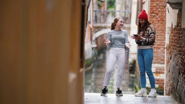 二人の若い女性が電話を見ている。ヴェネツィアの路上で. - 写真・画像