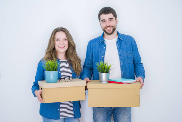 Young beautiful couple holding cardboard boxes very happy for moving to a new home over white isolated background - Photo, Image