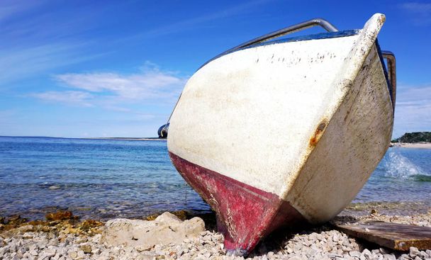 青い海と空を背景に小石のビーチで立ち往生した古い損傷ボートの弓 - 写真・画像