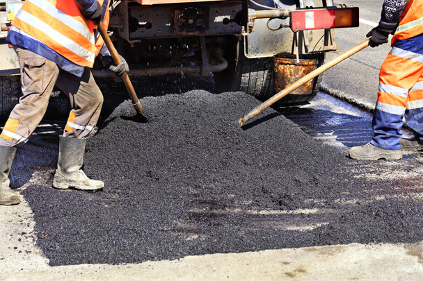 De werkende bemanning verdeelt gelijkmatig warm asfalt met schoppen handmatig op de gerepareerde plaats van de weg. - Foto, afbeelding