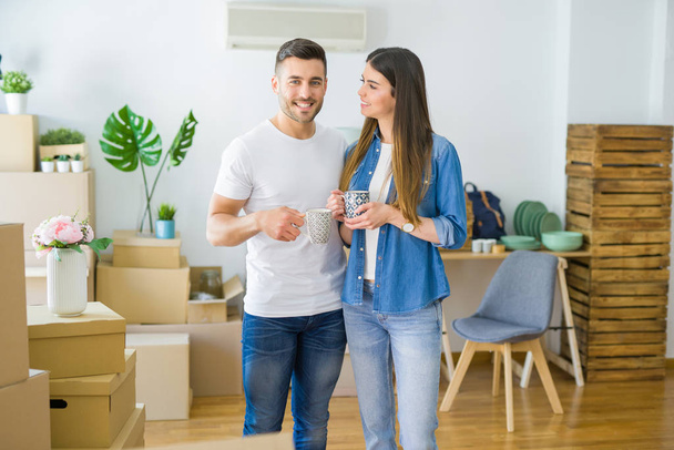 Hermosa pareja mudándose a una nueva casa, sonriendo alegre bebiendo una taza de café
 - Foto, Imagen