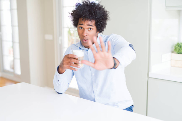 Uomo afro-americano con capelli afro bere una tazza di caffè a mano aperta facendo stop segno con espressione seria e fiduciosa, gesto di difesa
 - Foto, immagini