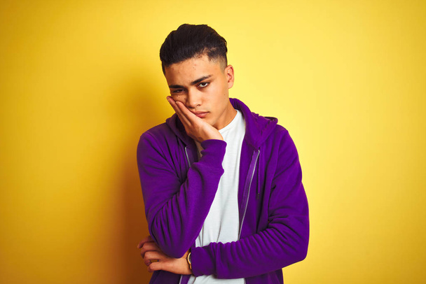 Young brazilian man wearing purple sweatshirt standing over isolated yellow background thinking looking tired and bored with depression problems with crossed arms. - Photo, Image