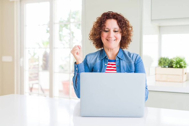 Senior vrouw werken met behulp van computer laptop schreeuwen trots en het vieren van overwinning en succes zeer opgewonden, juichen emotie - Foto, afbeelding