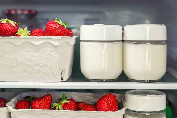 Ράφι ψυγείου με οργανικές ζουμερές φράουλες σε βιολογικά ανακυκλωμένα χάρτινα κουτιά και σπιτικό φυσικό γιαούρτι γάλακτος. Ψυγείο γεμάτο μούρα σε δοχεία από χαρτόνι. Υγιεινή και φιλική προς το οικολογικό φαγητό διατροφή - Φωτογραφία, εικόνα