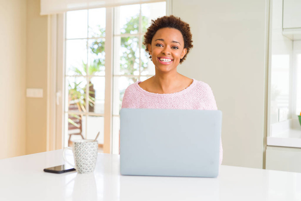 Νεαρή αφρικανική Αμερικάνικη γυναίκα που εργάζεται χρησιμοποιώντας φορητό υπολογιστή με ένα χαρούμενο και δροσερό χαμόγελο στο πρόσωπο. Τυχερός άνθρωπος. - Φωτογραφία, εικόνα