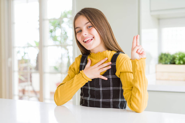 Młoda dziewczyna Piękna Blondynka ubrana casual żółty sweter w domu uśmiechnięta przeklinanie ręką na klatce piersiowej i palce w górę, co obietnicy lojalność obietnica - Zdjęcie, obraz