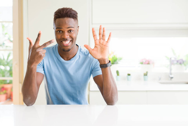 Handsome african american man wearing casual t-shirt at home showing and pointing up with fingers number eight while smiling confident and happy. - Фото, зображення