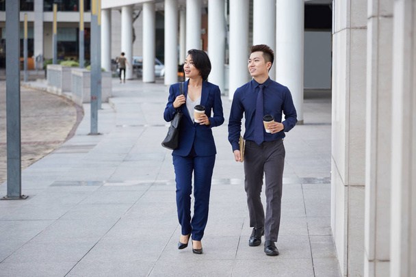 Asiático jovens parceiros de negócios andando na cidade juntos falando e bebendo café de copos descartáveis
 - Foto, Imagem