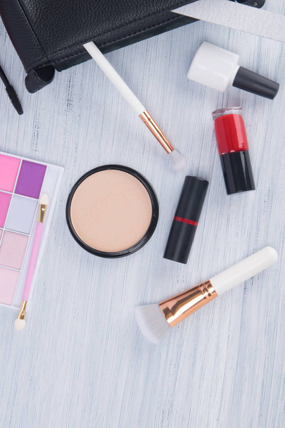 on a light background scattered items for makeup and manicure, multi-colored eye shadow, face powder with brushes, nail polishes and lipstick - Fotó, kép