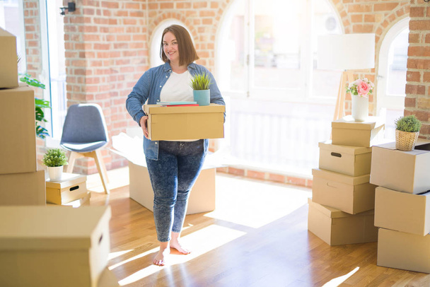 Young beautiful plus size woman moving to a new house, holding cardboxes smiling very happy for new apartment - Photo, Image