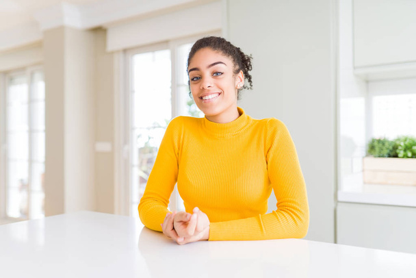 Beautiful african american woman with afro hair wearing a casual yellow sweater with hands together and crossed fingers smiling relaxed and cheerful. Success and optimistic - Foto, Bild
