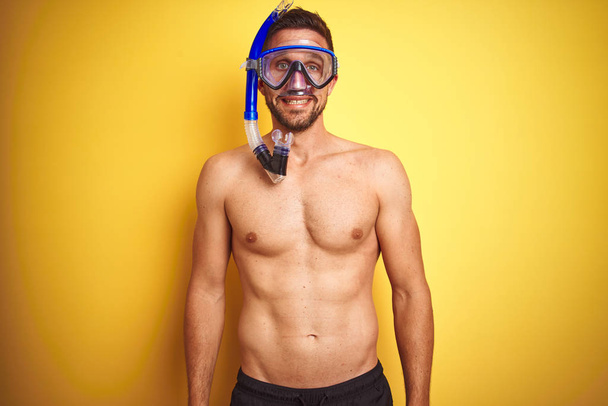 Young handsome shirtless man wearing diving goggles over isolated yellow background with a happy face standing and smiling with a confident smile showing teeth - Photo, Image