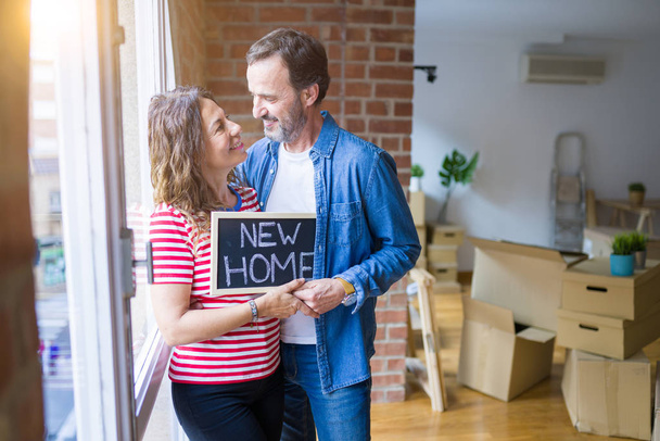 Middelbare leeftijd Senior paar verhuizen naar een nieuw huis, glimlachend blij verliefd op apartmant met een Blackboard met nieuwe huis tekst - Foto, afbeelding